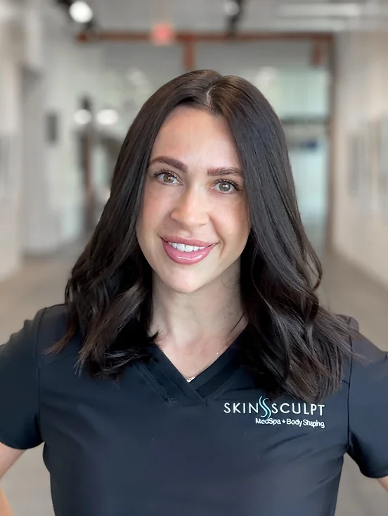 Portrait of Cami Heiner, smiling and wearing a black uniform with 'SkinSculpt Medspa & Body Shaping' logo, standing in a well-lit hallway.