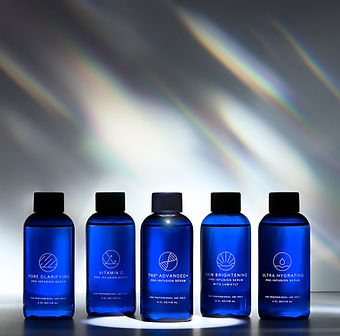 Five blue bottles of skincare serums lined up in a row with a gradient background.