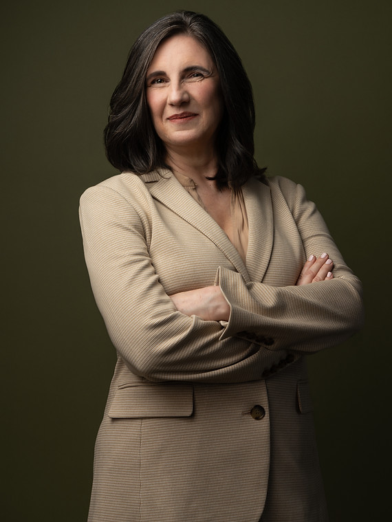 Portrait of Dr. Julie A. Maughan, a woman with shoulder-length dark hair, wearing a beige blazer, standing with arms crossed and smiling.